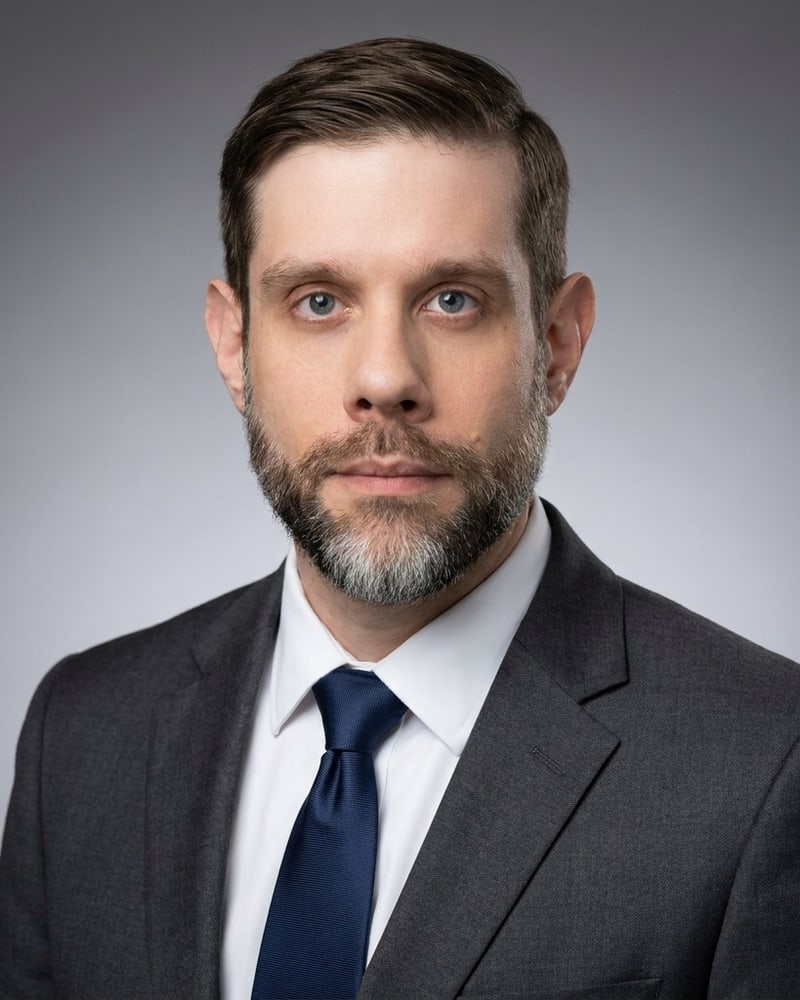 Tony Sharon, studio headshot in a charcoal suit and navy tie, looking straight at the camera.