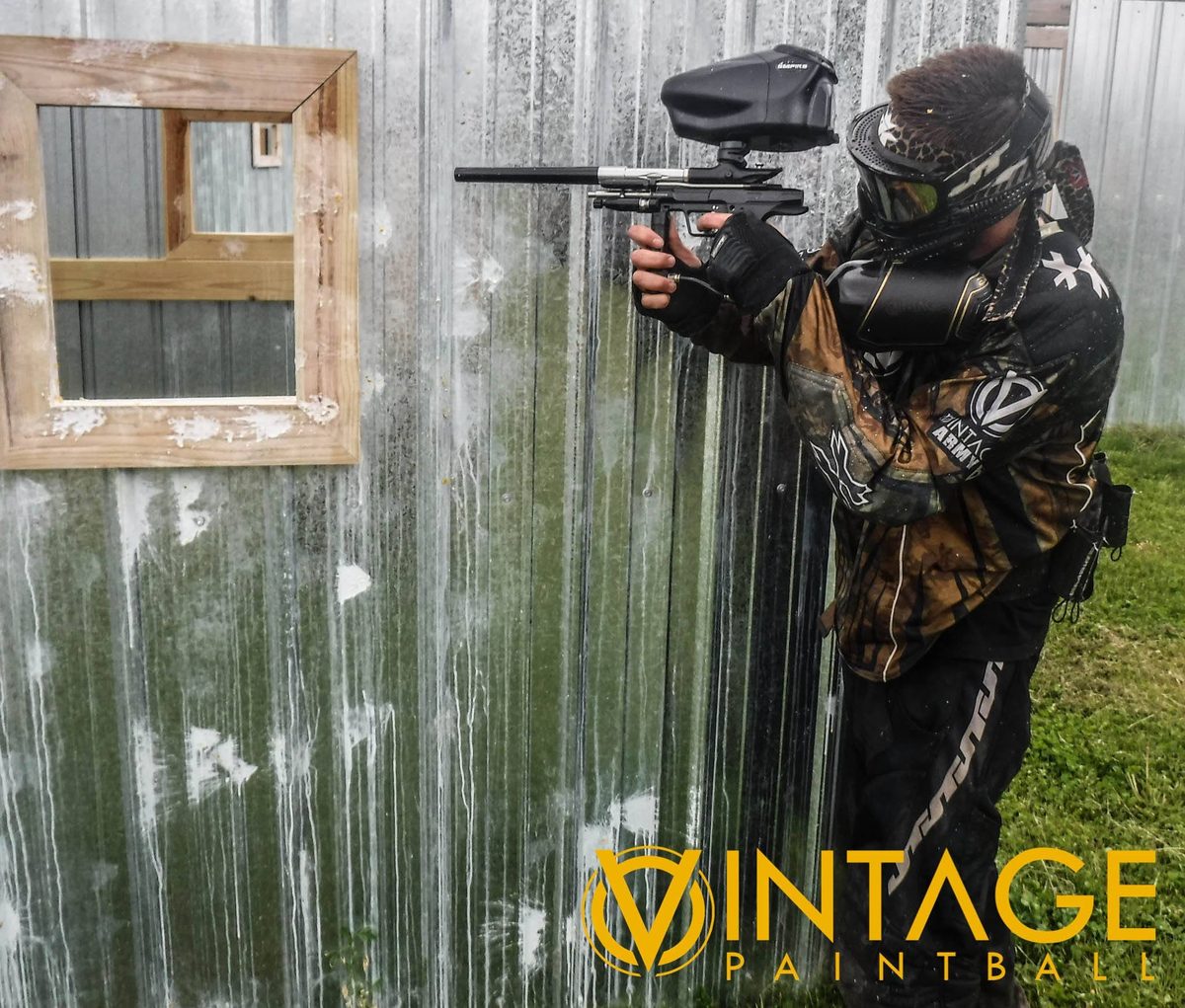 Tony, in Vintage Army camo, aims past a window cut in a corrugated wall, May 2015.