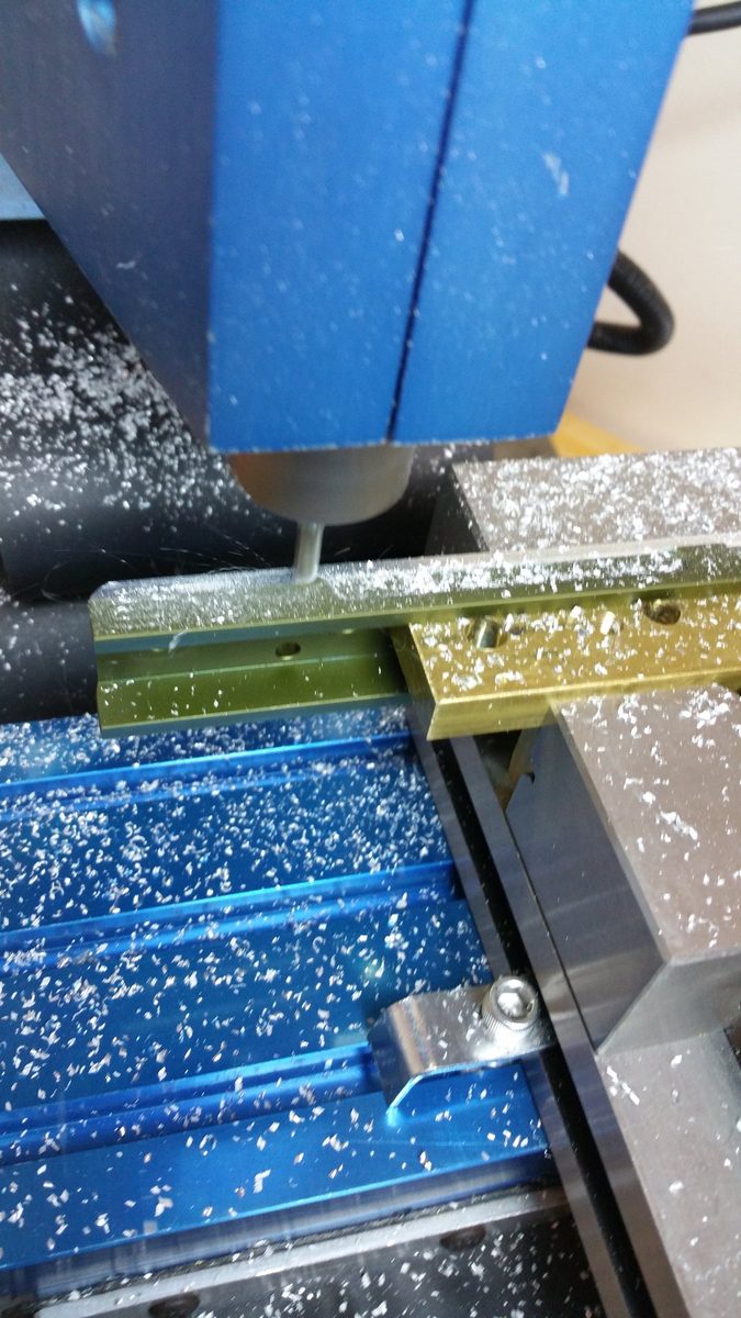 An end mill cutting a part on the MaxNC 10 benchtop CNC mill, chips piled across the vise and table.