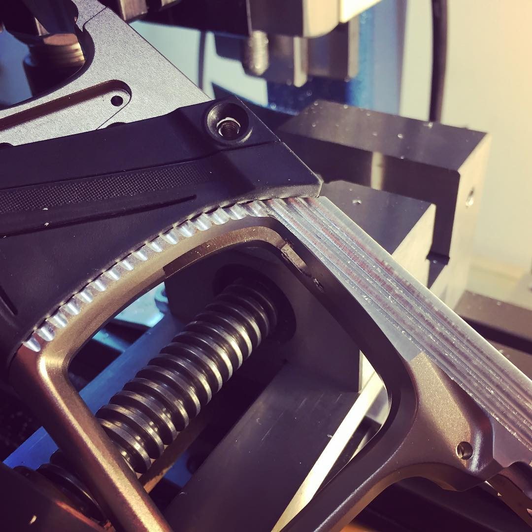 A marker grip frame clamped on the mill, its trigger guard freshly cut into a scalloped edge.